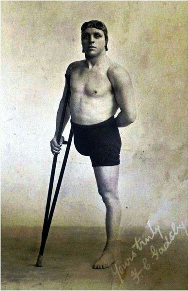 Frank Gadsby standing on one leg in swimming trunks, holding a crutch, with goggles on his cap. Signed Yours truly, F. C. Gadsby.